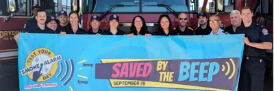 Firefighters standing with a banner that says "saved by the beep"