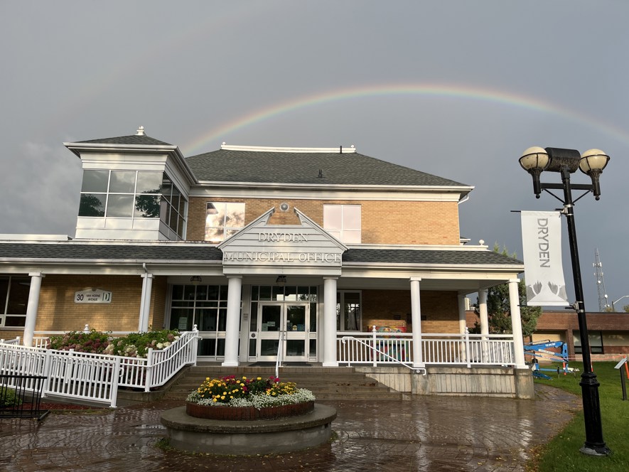 City Hall after a rainstorm with a rainbow in the dark sky behind it.
